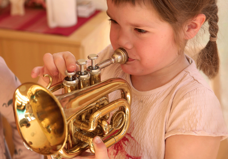 Ein Mädchen mit Zöpfen spielt Trompete. Foto: PädSek/ Charlotte Fischer