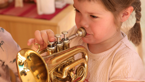 Ein Mädchen mit Zöpfen spielt Trompete. Foto: PädSek/ Charlotte Fischer.