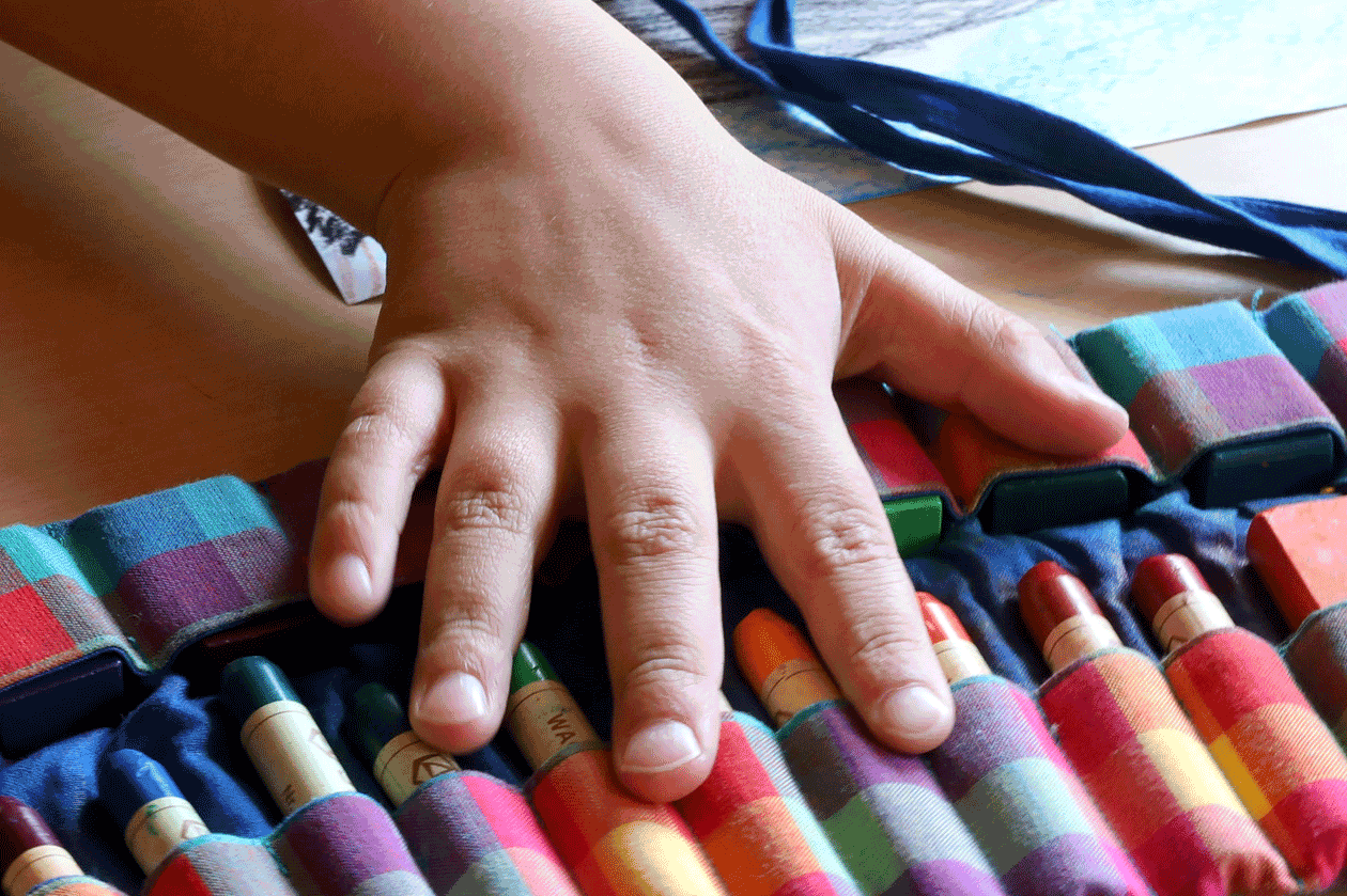 Eine Kinderhand über Wachsmalstifte (Bild: PädSek/Charlotte Fischer)